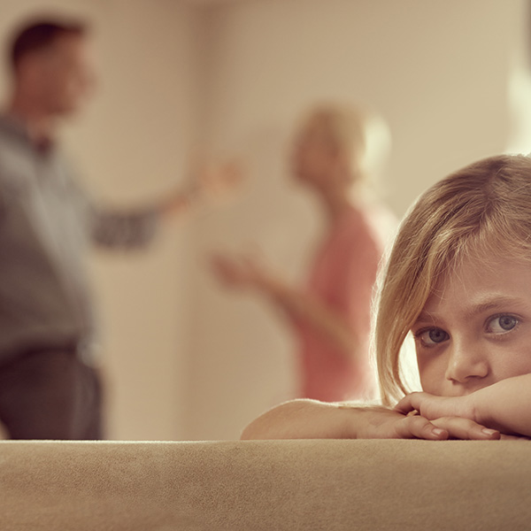 Childs seeing with a unhappy face while parents are fighting in the background